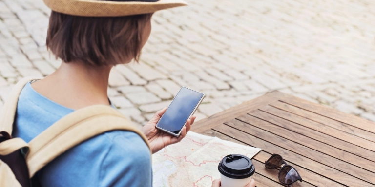 Young woman with map and coffee cup holds mobile 